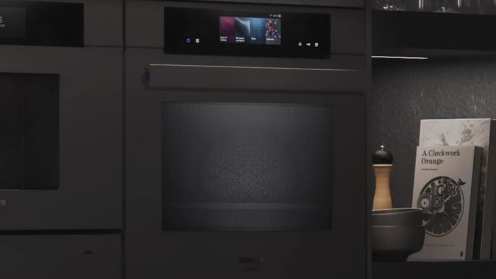 Een slanke zwarte Siemens oven met een digitaal display, vergezeld van een pepermolen, kommen en een boek met de titel "A Clockwork Orange."   