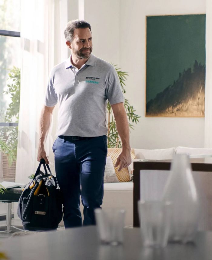 Tecnico in uniforme Siemens che entra in un soggiorno luminoso con una borsa degli attrezzi