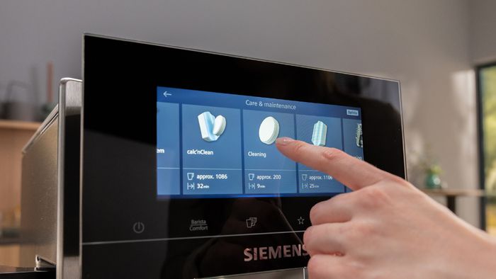 יד של אדם לוחצת על כפתור הניקוי בצג מכונת הקפה של סימנס