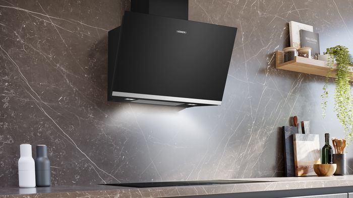 Cappa a parete Siemens nera inclinata, posizionata sopra il piano cottura a induzione 