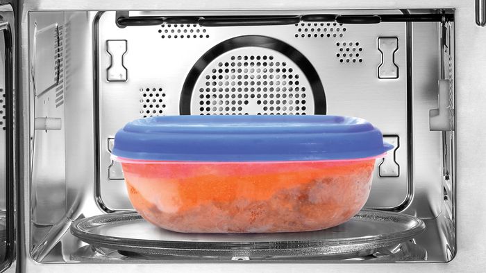 Ciotola in plastica con coperchio blu, contenente cibo al sugo, appoggiata sul piatto girevole del microonde