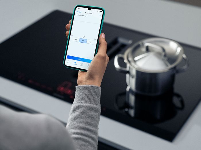 A person using a smartphone to control the power level of an induction cooktop with a pot on it.