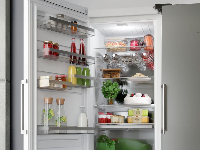 
       Int&eacute;rieur du r&eacute;frig&eacute;rateur Siemens : des &eacute;tag&egrave;res en verre soigneusement dispos&eacute;es avec des produits frais, des boissons, des produits laitiers et un tiroir &agrave; glace.
      