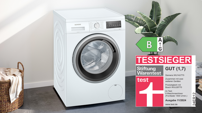 Die Testsieger Waschmaschine WU14UT70 steht in einem Raum vor einer wei&szlig;en Wand. Das Testsieger Logo ist neben der Waschmaschinen-Frontansicht abgebildet.