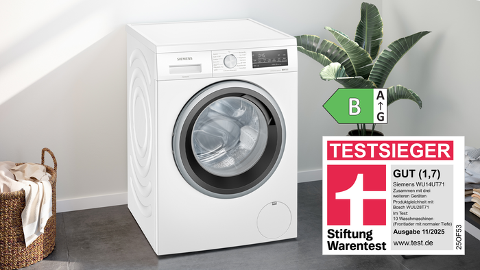 &bdquo;Siemens Waschmaschine WU14UT71 mit Stiftung Warentest Testsieger-Siegel GUT (1,7), Energielabel B und Hinweis &sbquo;Made in Europe&lsquo; in modernem Raum mit Pflanze und gefalteter W&auml;sche.