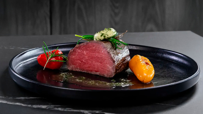 Angeschnittenes St&uuml;ck Rindfleisch auf schwarzem Teller mit Gem&uuml;se und Kr&auml;utern.