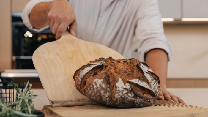 Frisch gebackenes Brot wird mit einem Holzschieber aus dem Siemens iQ700 Backofen in einer modernen K&uuml;che genommen.