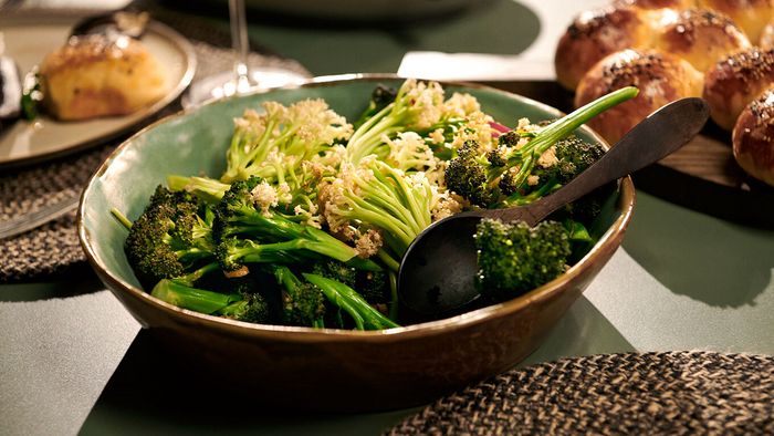 Tavola apparecchiata con ciotola di broccoli saltati e pane dorato sullo sfondo