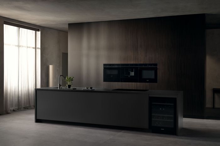 Cucina moderna minimalista dalle tonalit&agrave; scure con isola centrale ed elettrodomestici da incasso