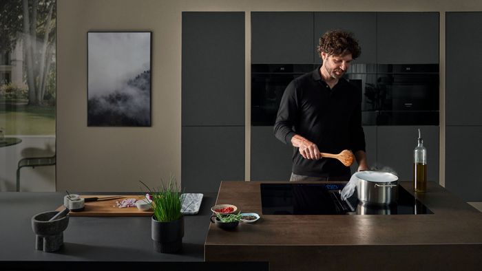 Uomo che cucina in una cucina moderna con isola in legno e pentola sul piano cottura a induzione