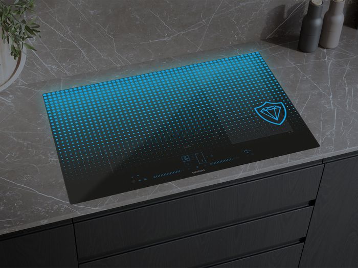 A black Siemens induction cooktop with a vibrant blue illuminated dotted pattern and a diamond shield logo, set into a dark marble countertop.