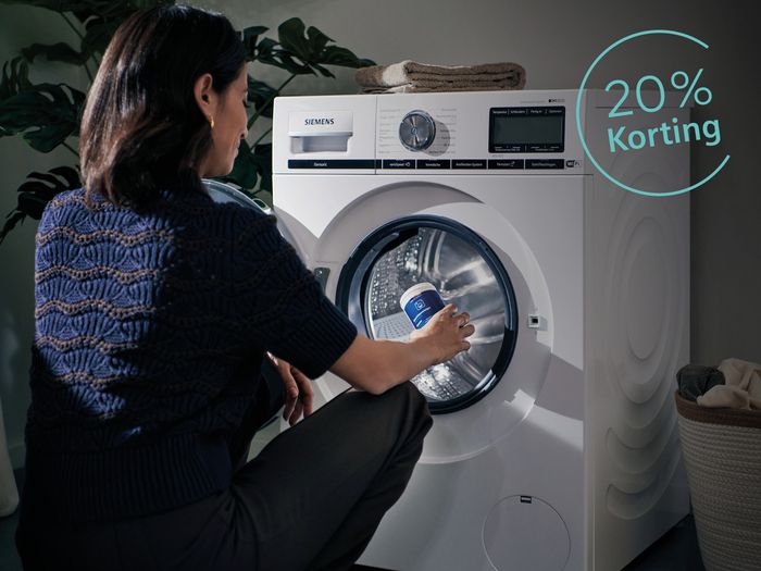 Vrouw zit voor wasmachine met reinigingsmiddel in haar had en stopt dit in de trommel