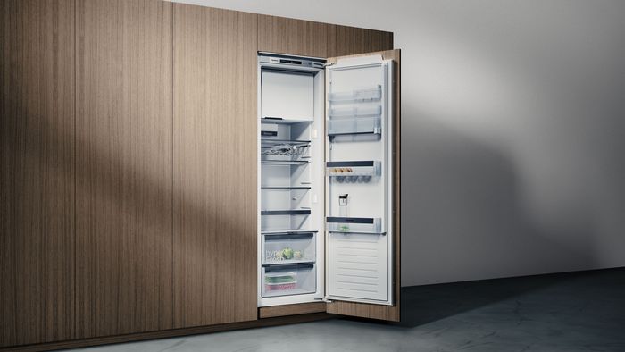 Frigorifero da incasso Siemens integrato in una cucina in legno, con sportello aperto e ripiani visibili con poche pietanze