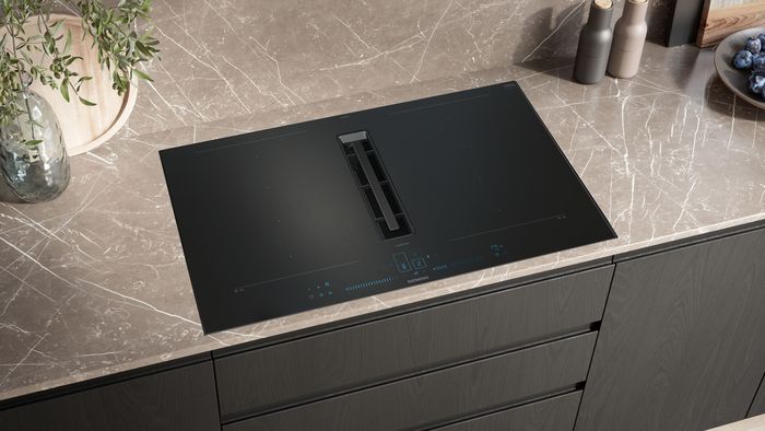 Piano cottura a induzione nero con cappa integrata su piano in marmo chiaro