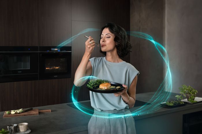 Persona en una cocina moderna sosteniendo un plato con salm&oacute;n y verduras, a punto de comer con un tenedor, rodeada por un efecto de remolino azul digital.