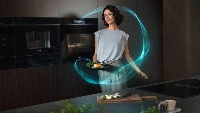 Eine Frau steht mit einem Gericht auf dem Teller vor einem Siemens iQ700 Backofen.