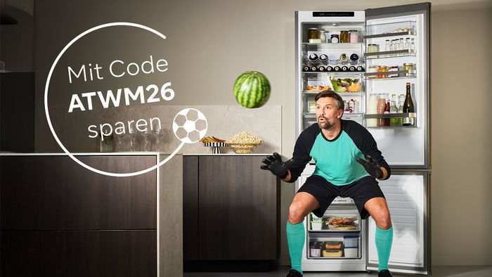 Mann in Fu&szlig;balltrikot und Torwartposition vor offenem K&uuml;hlschrank mit Lebensmitteln und Text 'Mit Code "ATWM26" sparen'