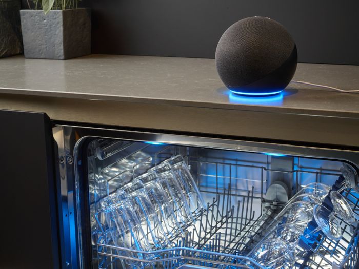 Lavastoviglie aperta con stoviglie all&rsquo;interno e smart speaker posizionato sul piano della cucina
