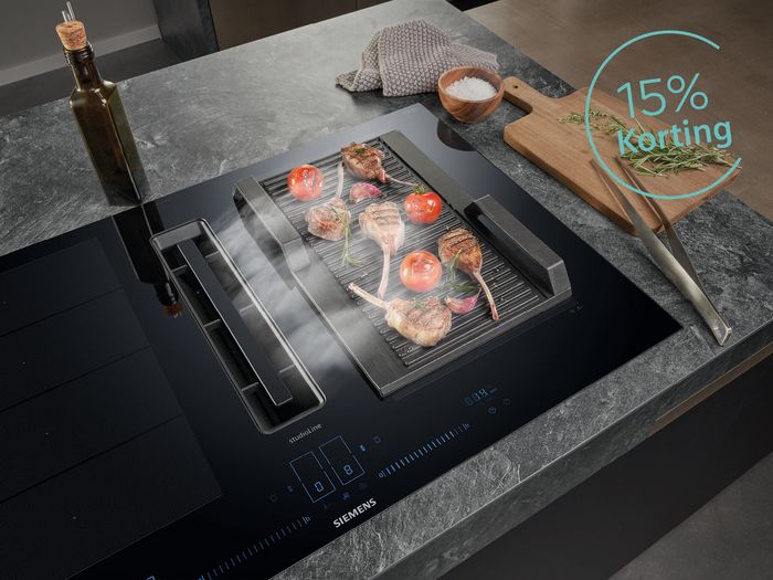 Siemens kookplaat met daarop een grillplaat met lamskoteletjes en tomaat. Aan zijkant olie en houtenplank
