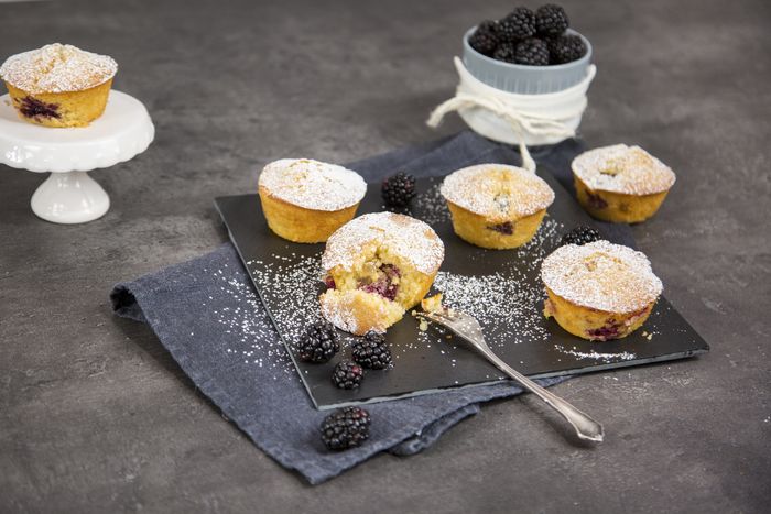 Mini muffin alle more con zucchero a velo su vassoio nero e ciotolina con more fresche sullo sfondo