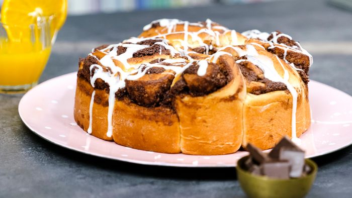 Dolce con glassa bianca su piatto rosa, con succo d&rsquo;arancia e ciotolina di cioccolato sullo sfondo