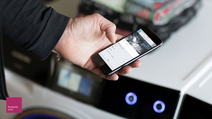 Un usuario sigue el ciclo de su lavadora y secadora inteligentes iQ700 de Siemens en la pantalla de su m&oacute;vil con la app Home Connect