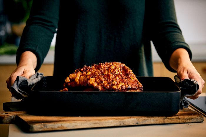 Persona che regge una teglia con arrosto appena sfornato, appoggiata su tagliere in cucina