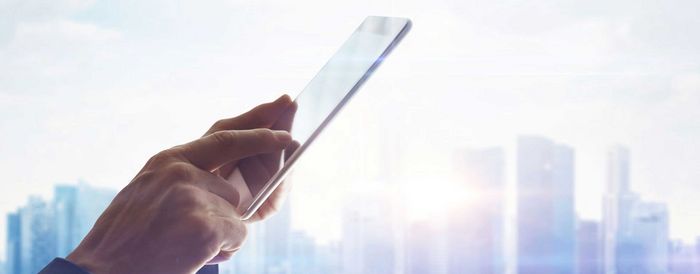 Una persona consulta en su tablet el manual de instrucciones de su electrodoméstico. Al fondo se intuye el skyline de una ciudad. 