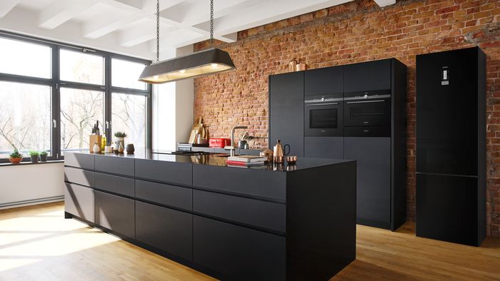 Eine schwarze Küche im Industrial Style mit freistehendem schwarzen Kühlschrank.