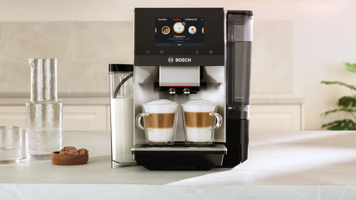 A modern Bosch coffee machine brews two cups of layered coffee drinks, featuring a touch display and milk container on a sleek countertop.