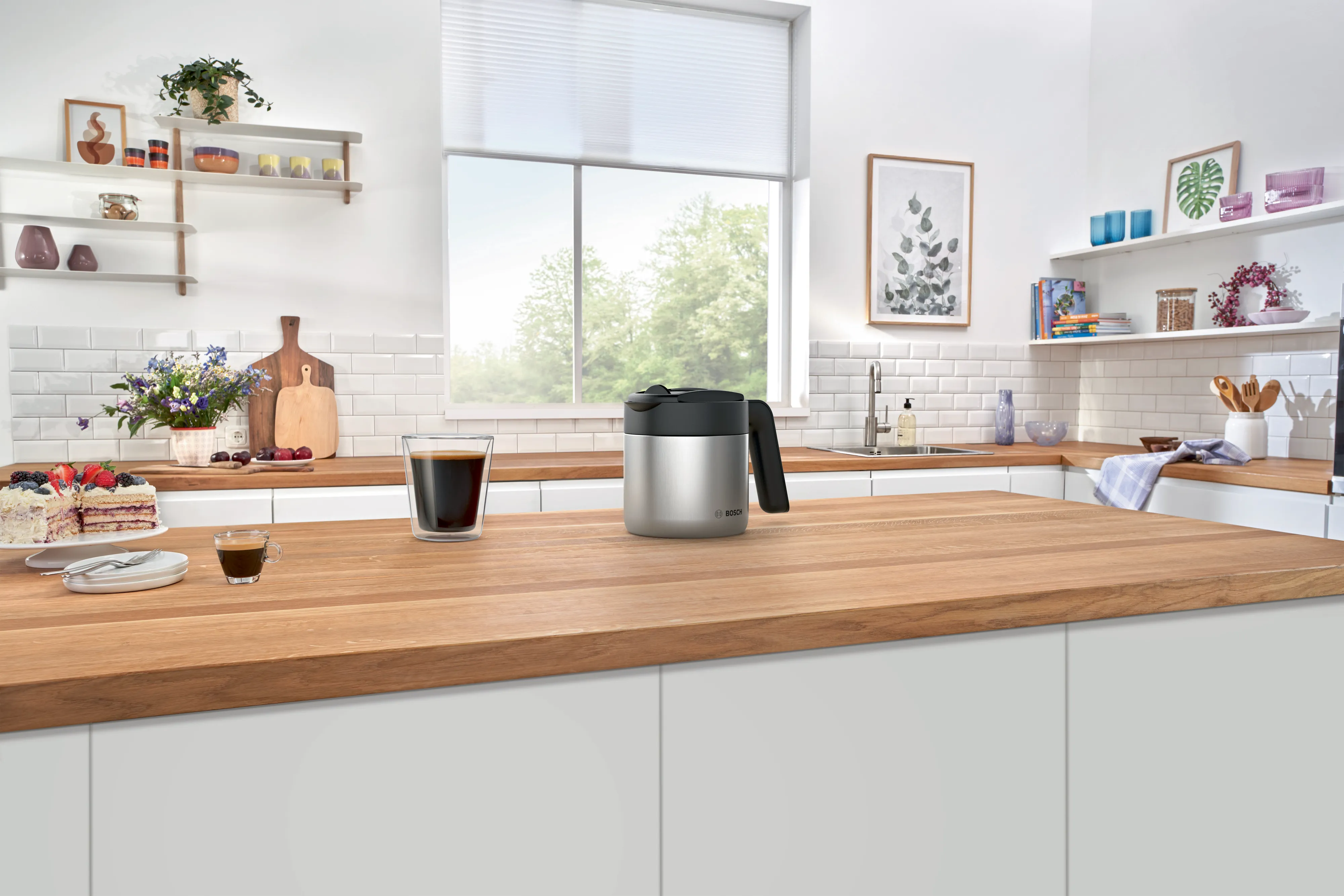 Cuisine moderne avec plan de travail en bois clair, cafetière noire et argent posée au centre, fenêtre lumineuse en arrière-plan