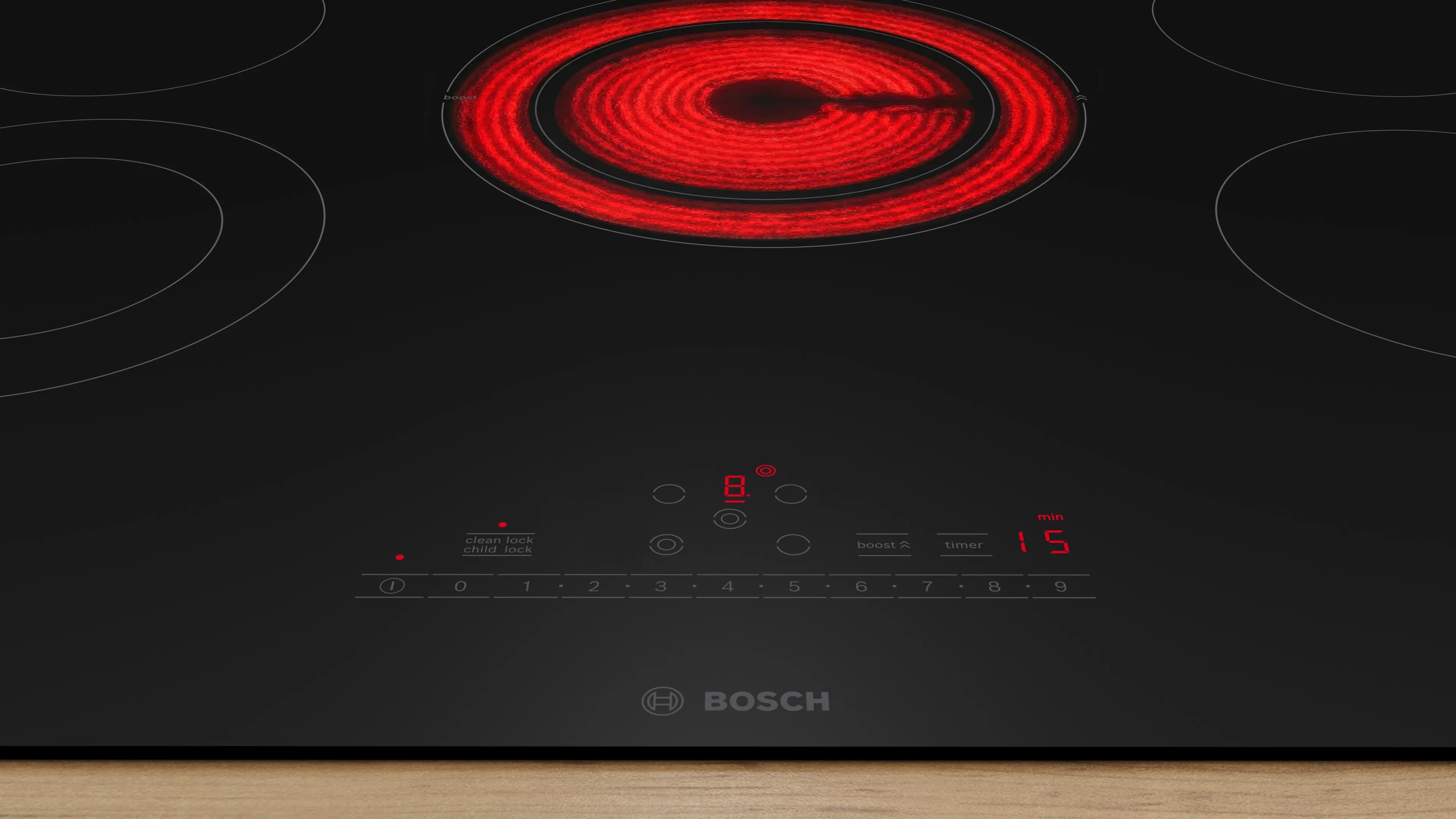 Black Bosch induction cooktop with a glowing red circular burner and touch controls on a wooden countertop.