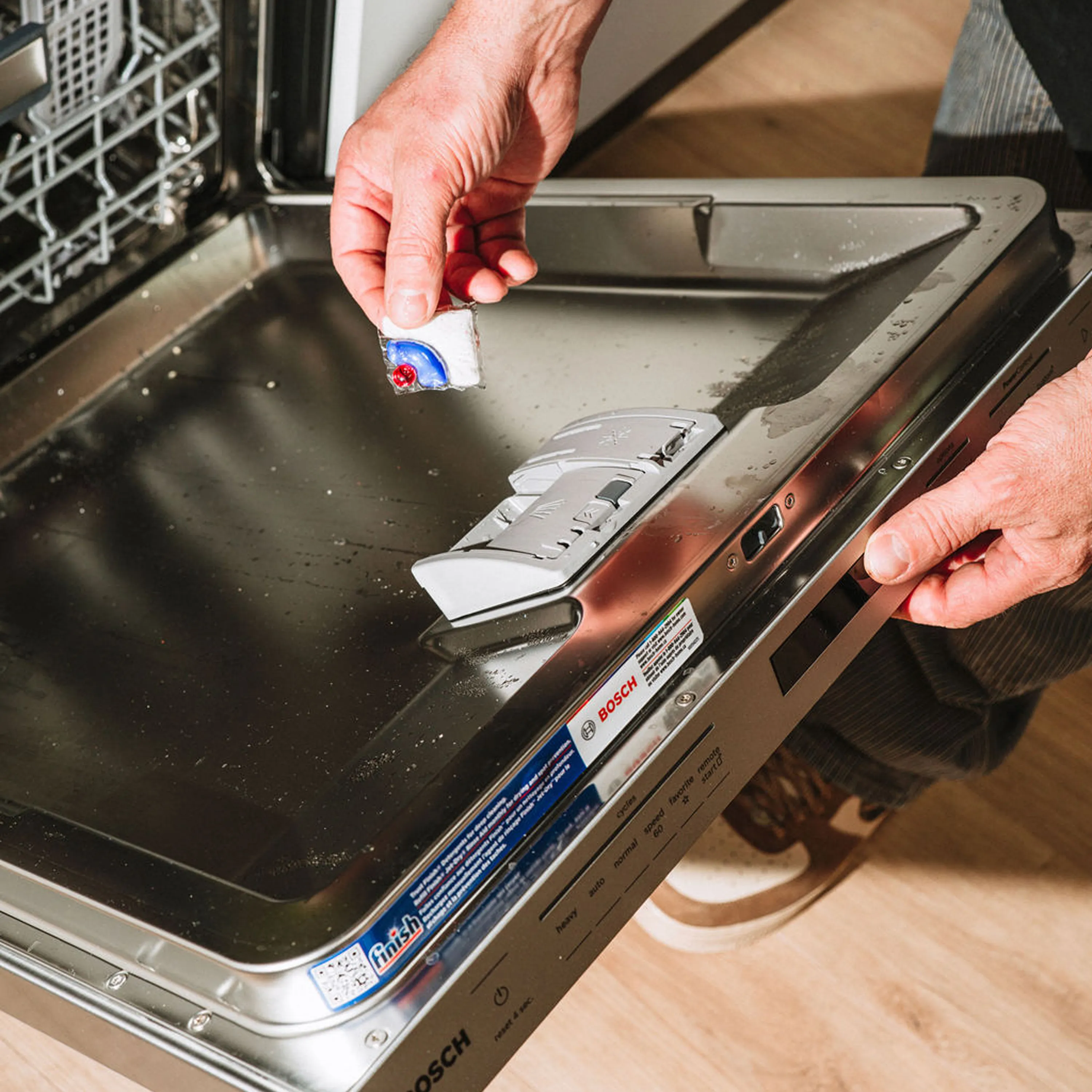 Person placing a detergent tablet into the detergent compartment of a Bosch dishwasher.