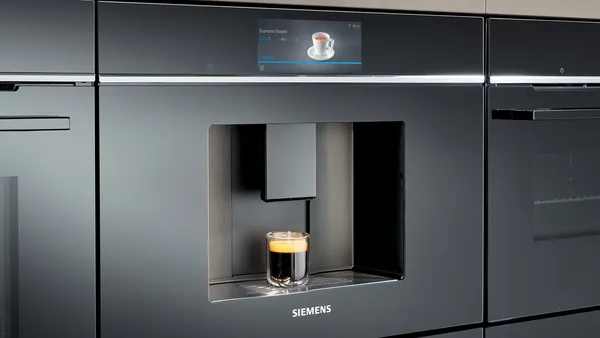 Siemens built-in coffee machines on a kitchen counter, each with a latte glass under the spout and digital displays showing coffee images.
